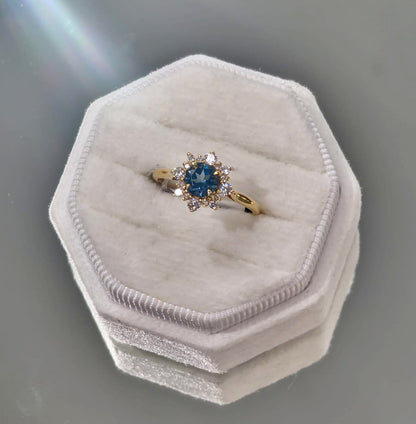 Gold ring with a blue gemstone on a white hexagonal cushion against a gray background